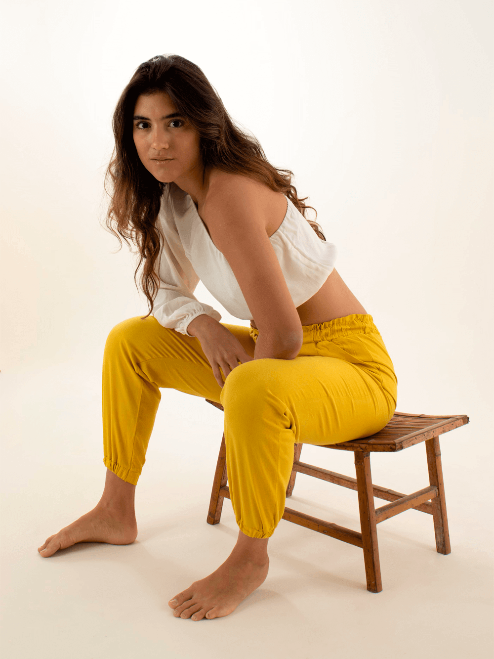 Modelo usando calça jogger Catarina amarela da marca Greenish, sentada em uma cadeira de madeira.