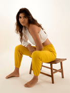 Modelo usando calça jogger Catarina amarela da marca Greenish, sentada em uma cadeira de madeira.