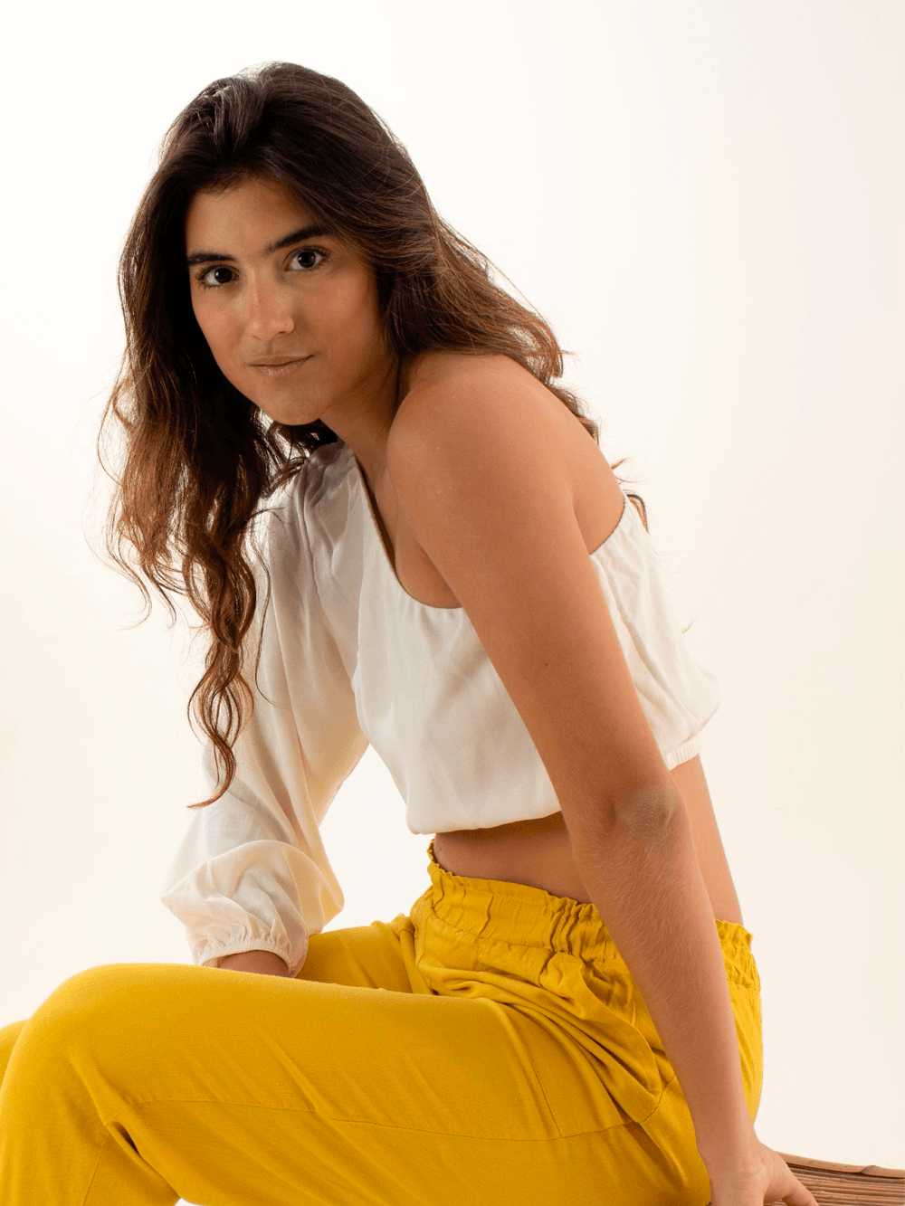 Modelo usando a blusa Tati off white da marca Greenish, combinando com calças amarelas em fundo neutro.