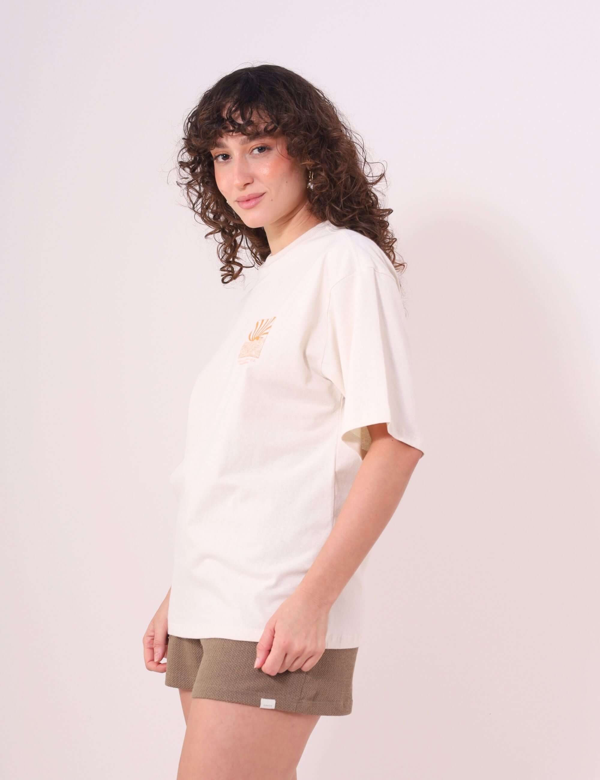 Mulher vestindo Camiseta Oversized Sunset Session Greenish, cor natural, com estampa de pôr do sol e ondas. Estilo confortável e descontraído.