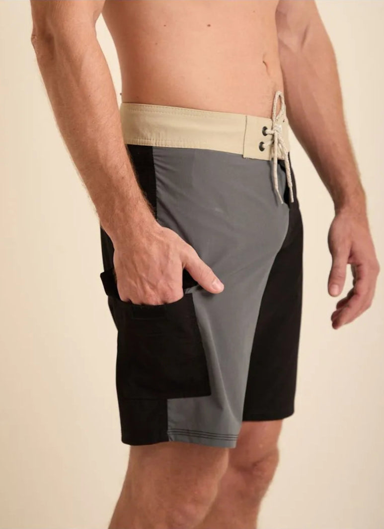 Modelo masculino vestido com bermuda de banho em tons de cinza e preto, destacando seu design moderno.
