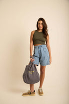 Modelo usando Bermuda Jeans Gih Azul da Greenish, com blusa verde e bolsa cinza, destacando estilo moderno e conforto.