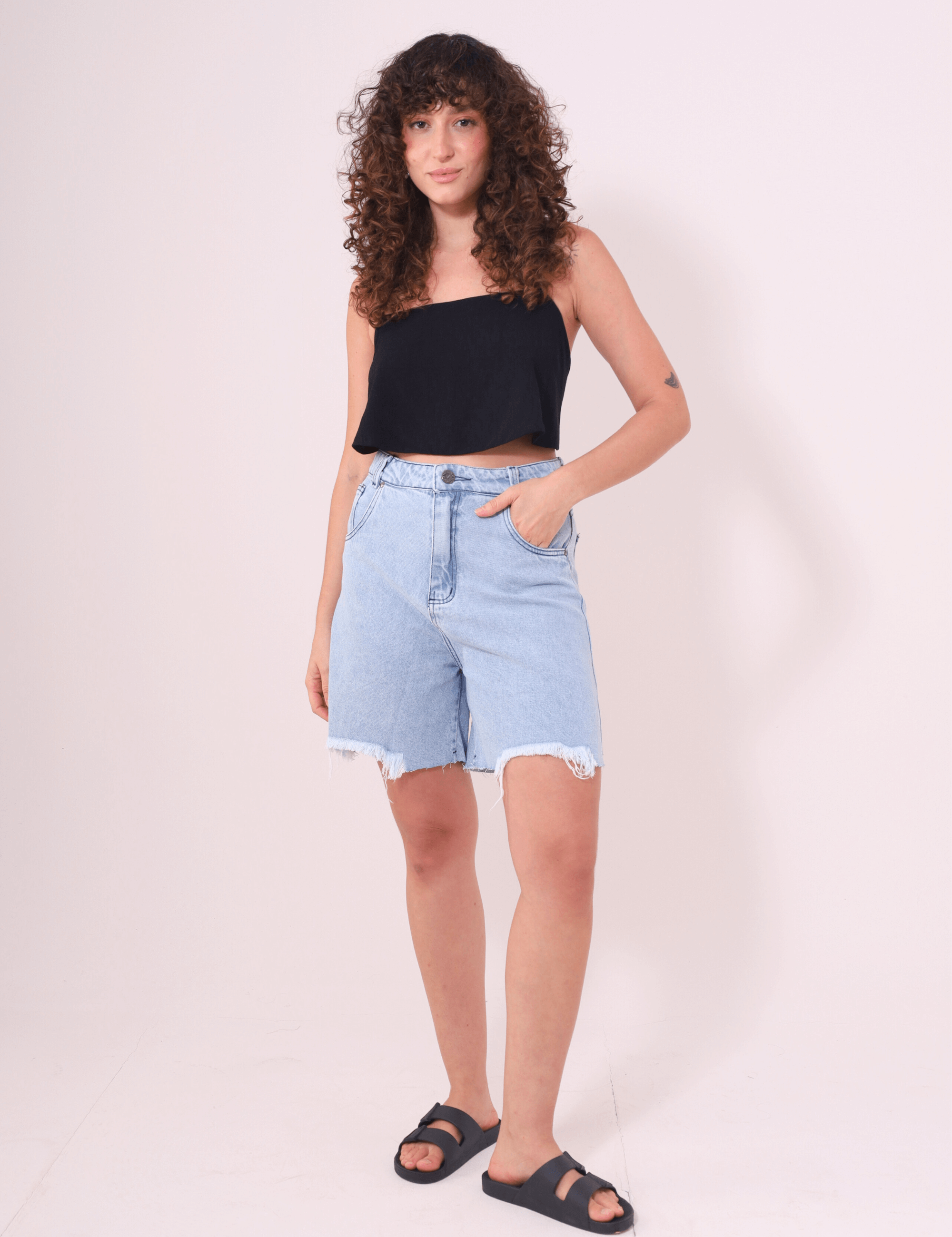 Mulher vestindo Bermuda Jeans Glicia Greenish, cintura alta, perna reta, caimento solto e acabamento desfiado, ideal para o verão.