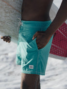 Sunga turquoise à beira da praia, surfista segurando prancha, estilo descontraído, moda de verão.