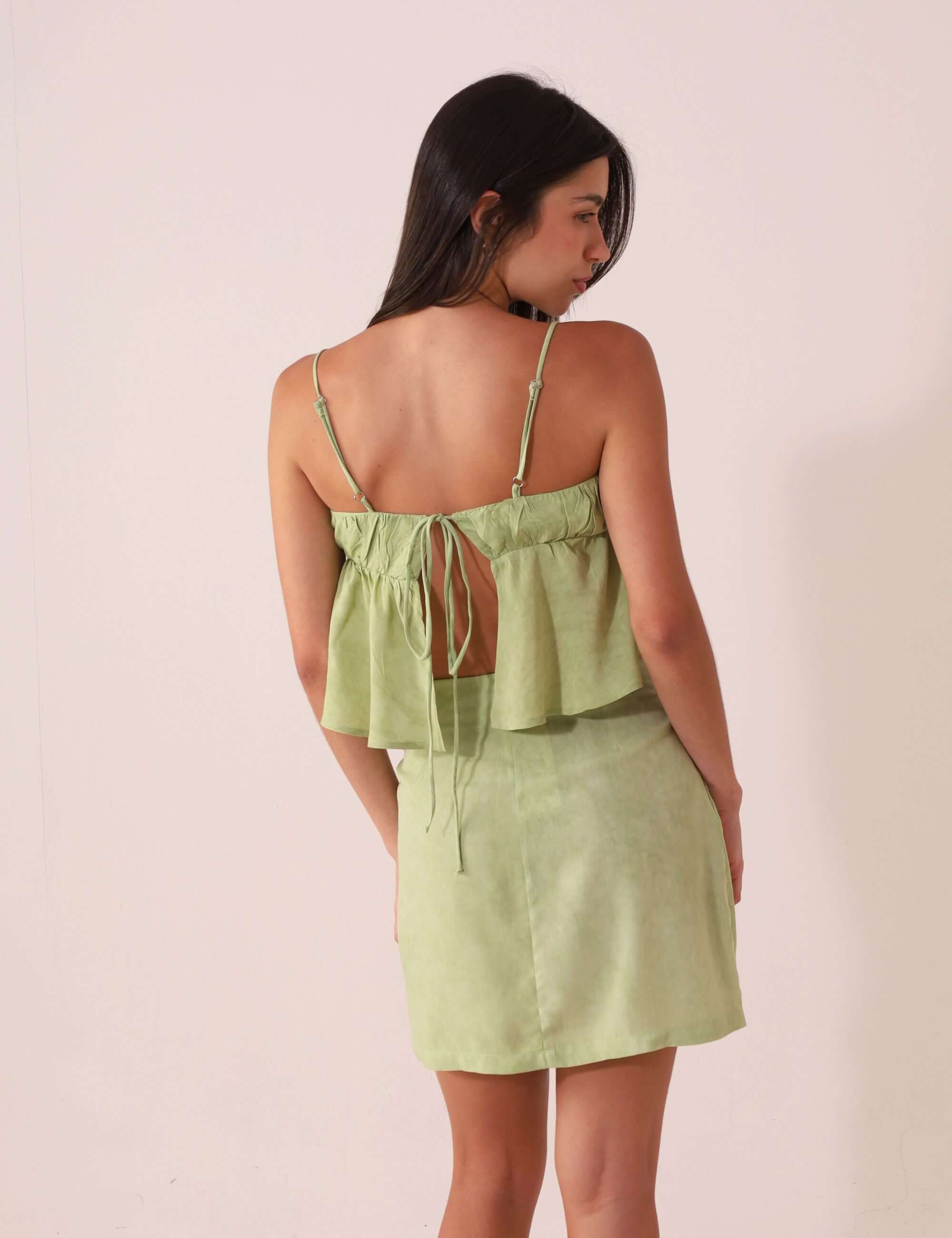 Mulher de costas vestindo a BLUSA THÁ - VERDE da Greenish, com alças finas e design romântico em viscose texturizada.