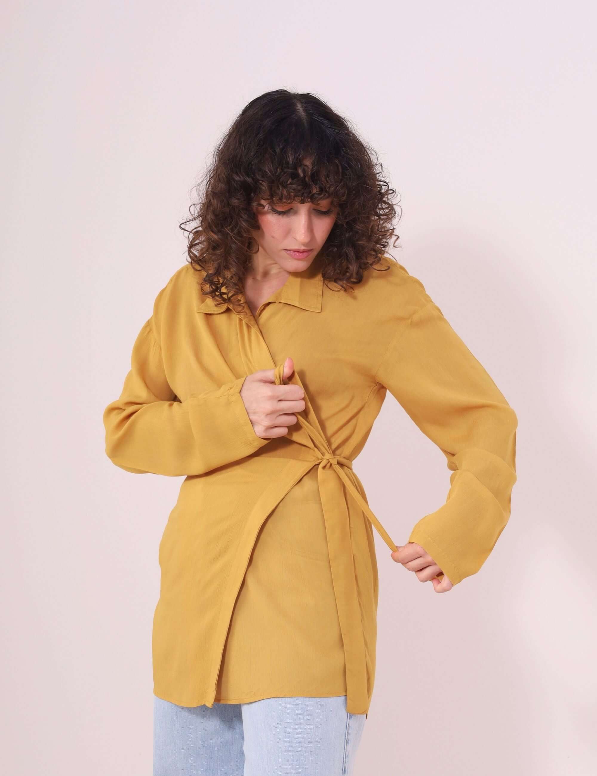 Mulher vestindo Blusa Kalu Mostarda da Greenish em viscose, com faixa na cintura e gola retrô, ideal para looks descomplicados.