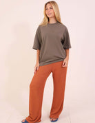 Mulher vestindo CALÇA MILA - MARROM da Greenish, modelagem reta e confortável com cintura alta em malha canelada marrom.