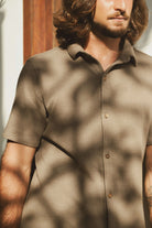 Homem vestindo Camisa Botão Maré - Verde Escuro com estilo casual e elegante, destacando-se em um ambiente ensolarado.