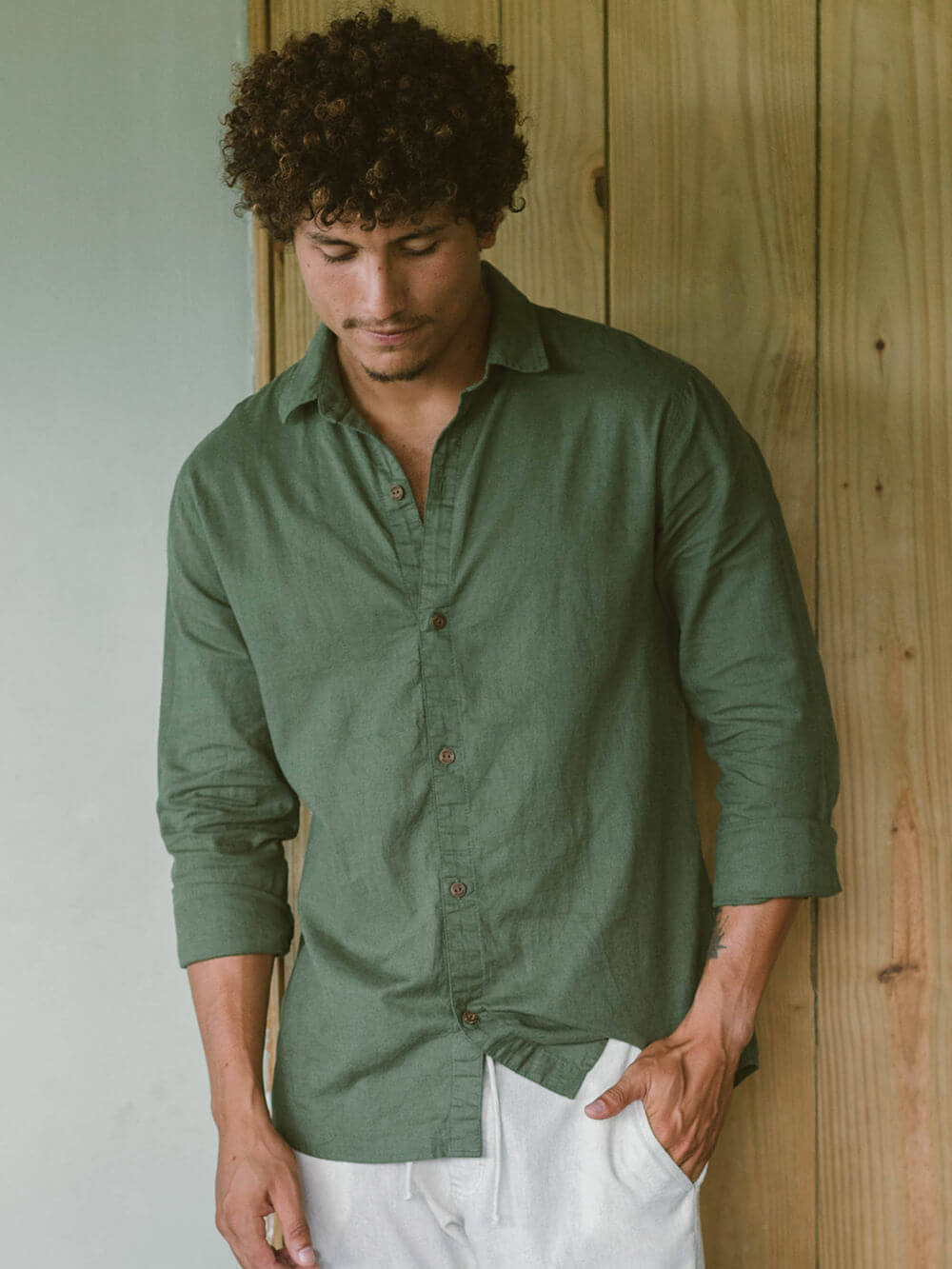 Homem usando camisa longa de linho verde da Greenish, com botões de coco, em cenário casual.