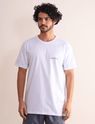 Homem vestindo camiseta branca Greenish Made By Surfers de algodão com estampa minimalista, ideal para uso diário e passeios na praia.