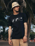 Camiseta preta Feel The Wind da Greenish, modelo clássico, estampa minimalista, em ambiente natural com palmeiras.