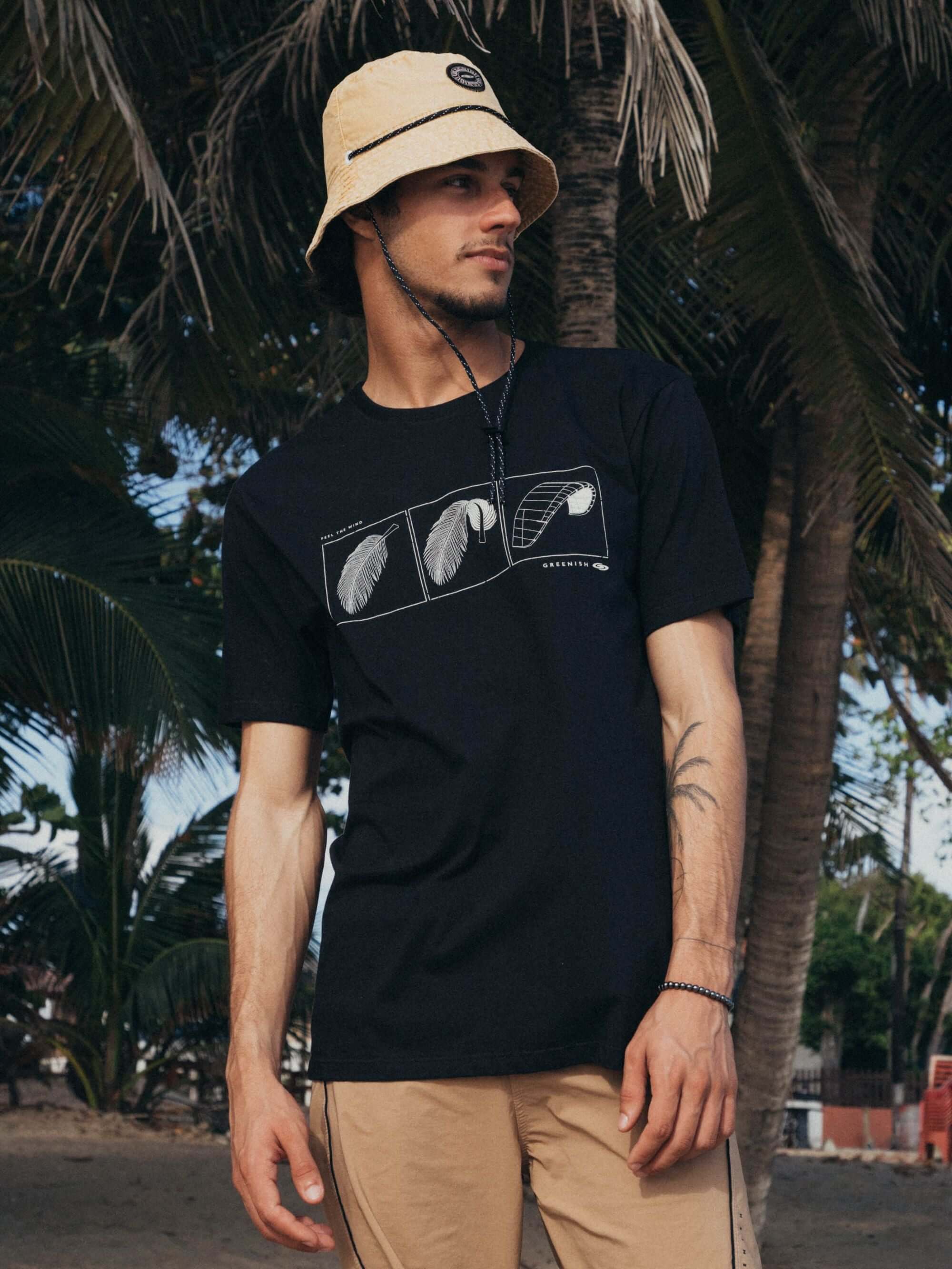 Camiseta preta Feel The Wind da Greenish, modelo clássico, estampa minimalista, em ambiente natural com palmeiras.