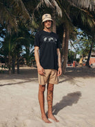 Modelo usando a camiseta Feel The Wind - Preto da Greenish, em ambiente praiano, com estilo descontraído.