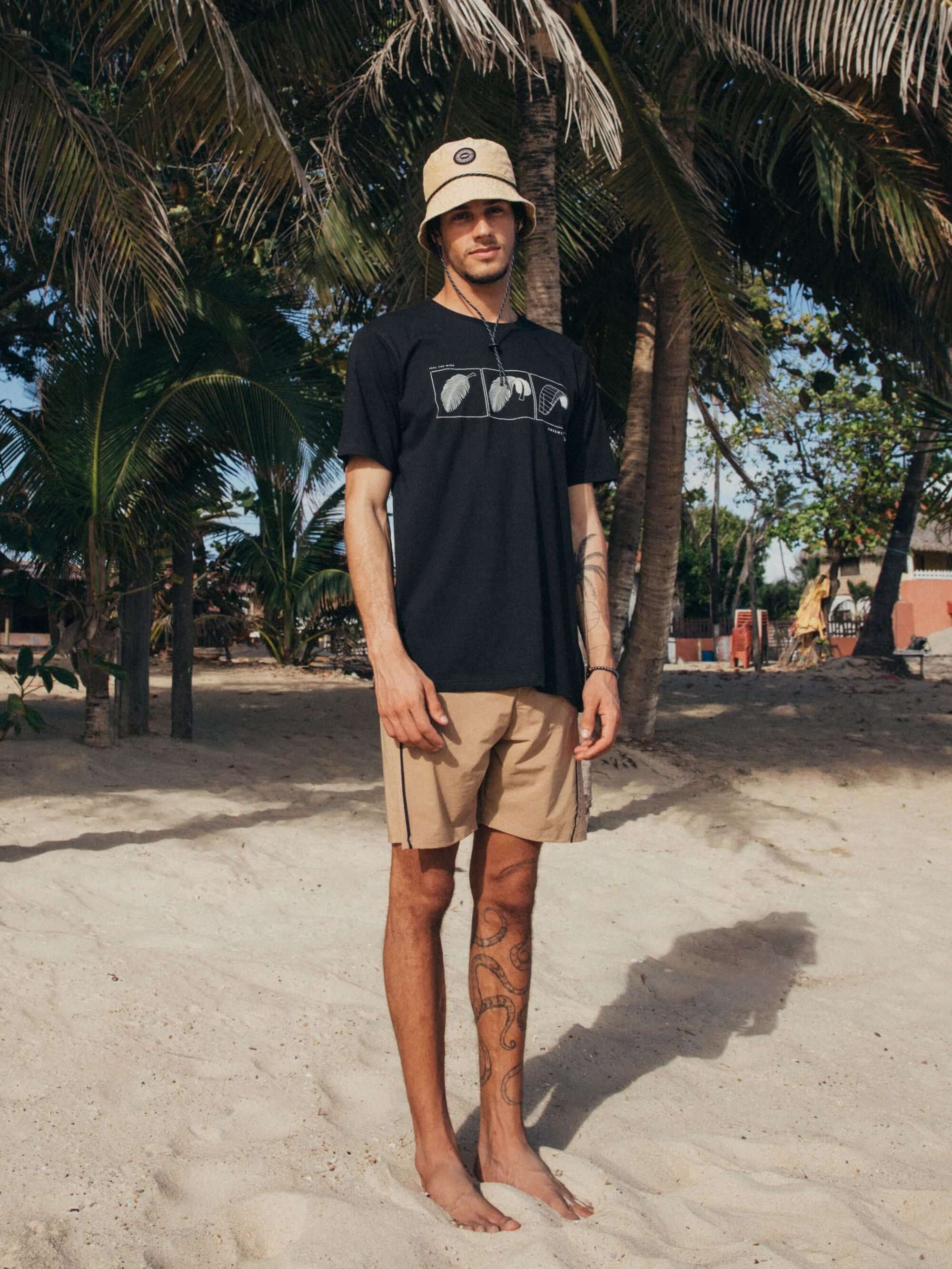 Modelo usando a camiseta Feel The Wind - Preto da Greenish, em ambiente praiano, com estilo descontraído.