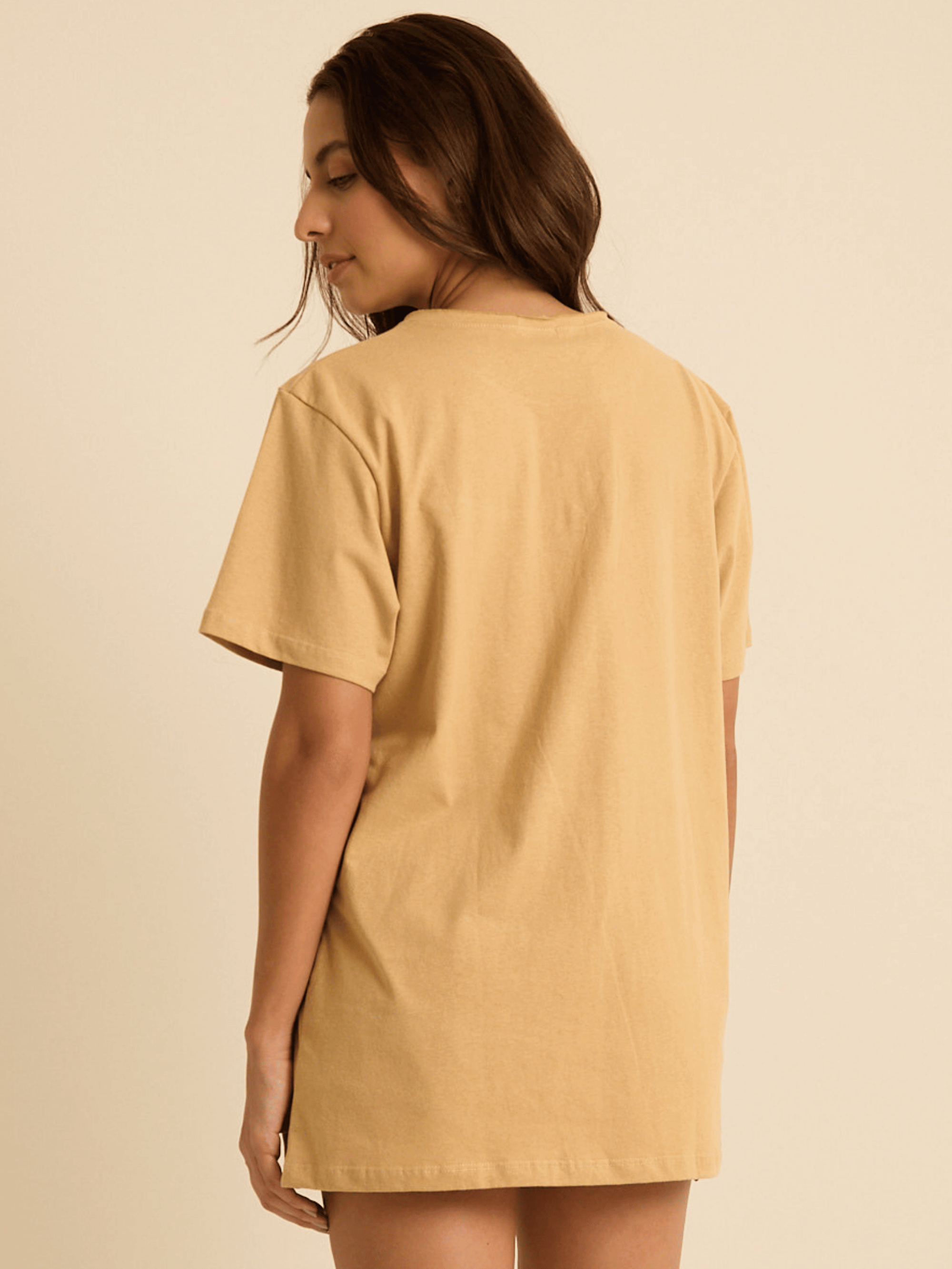 Modelo feminina usando camiseta oversized Siriguela bege da marca Greenish, vista de trás, em tecido 100% algodão.