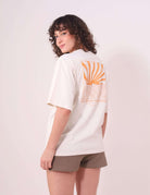 Mulher vestindo Camiseta Oversized Sunset Session - Natural da Greenish, com estampa de ondas e pôr do sol, em um look casual.