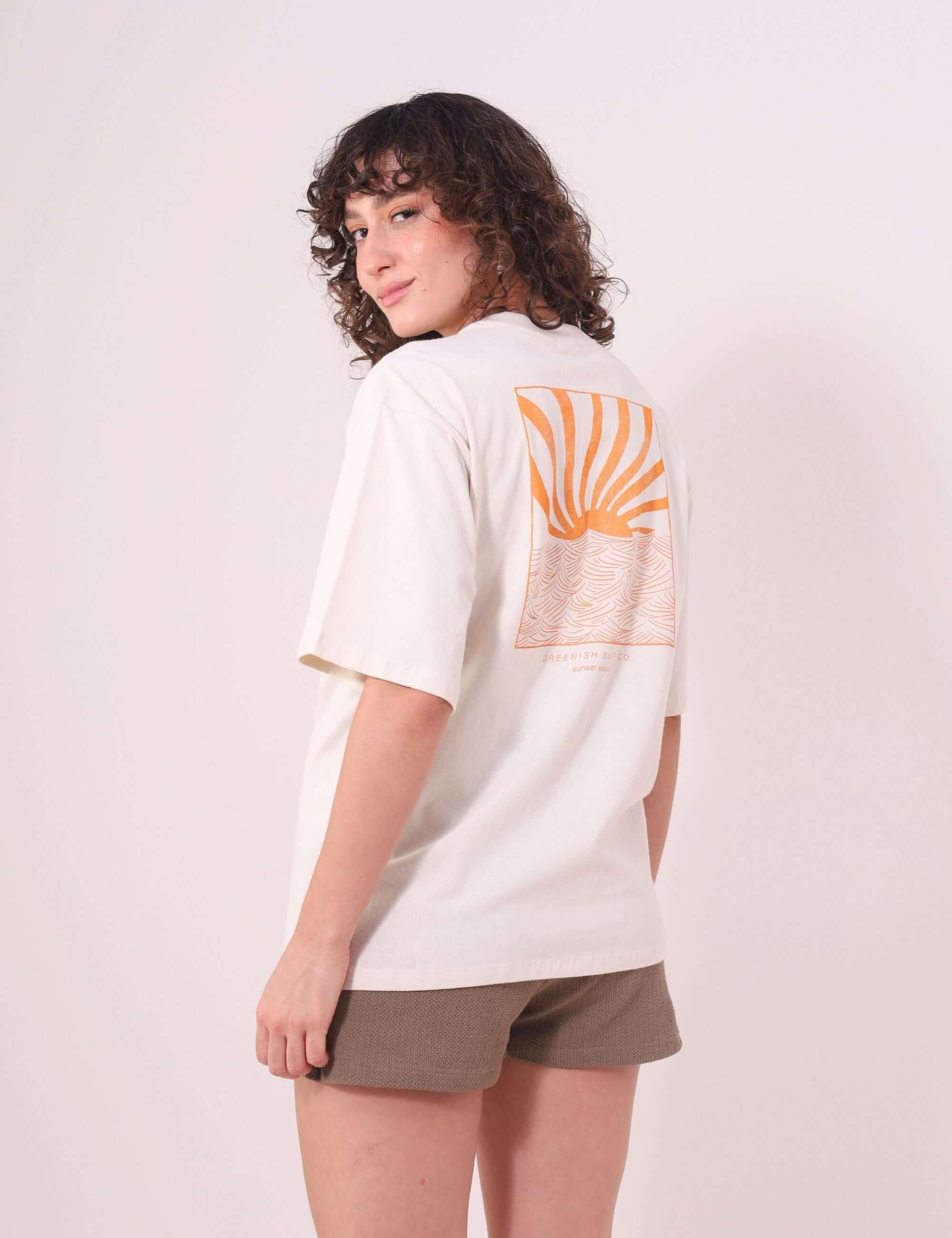 Mulher vestindo Camiseta Oversized Sunset Session - Natural da Greenish, com estampa de ondas e pôr do sol, em um look casual.
