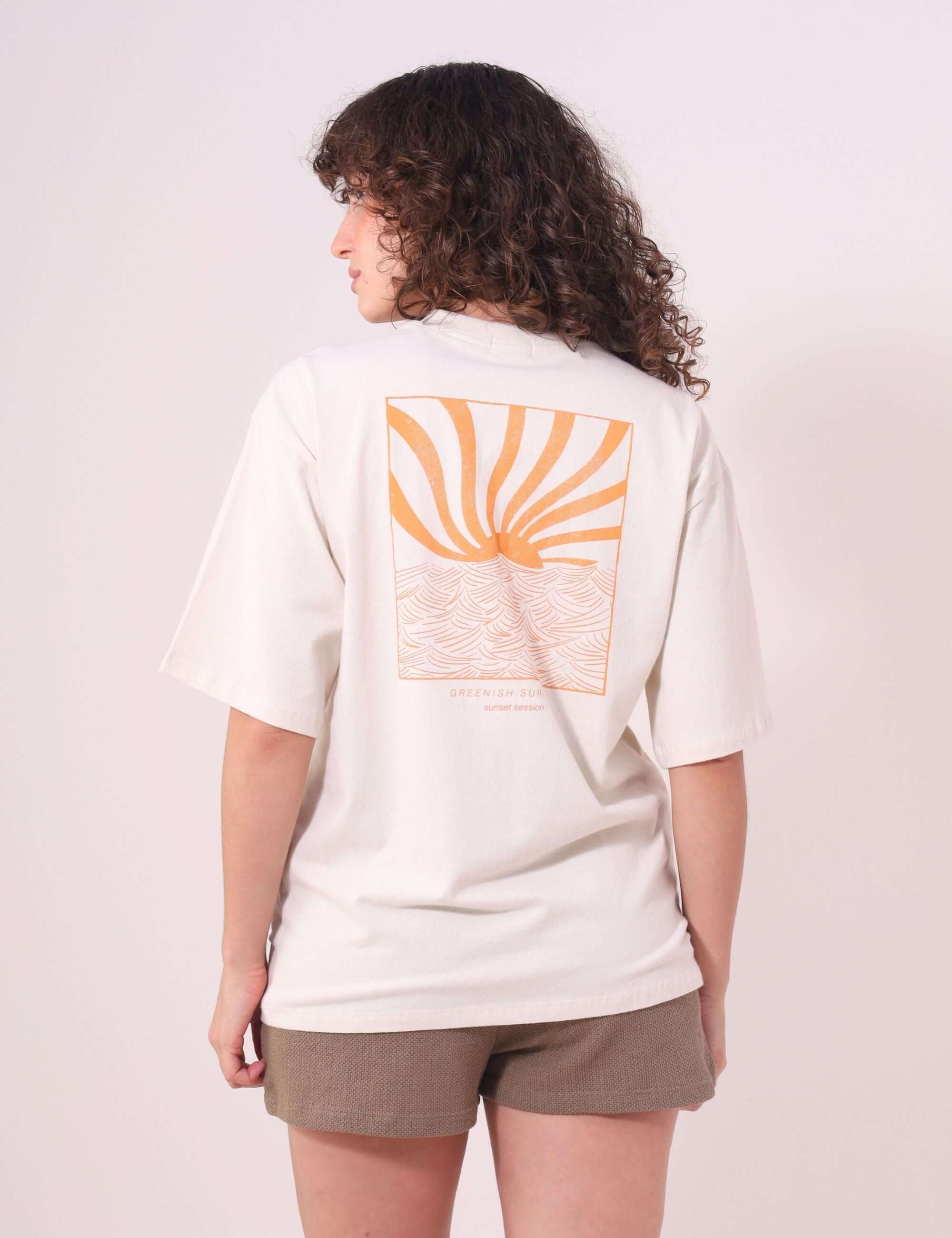Pessoa vestindo Camiseta Oversized Sunset Session Natural da Greenish, com estampa de ondas e pôr do sol nas costas.