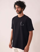 Modelo vestindo Camiserta Greenish Quality Product - Preto, com gola de ribana e silk frontal em relevo.