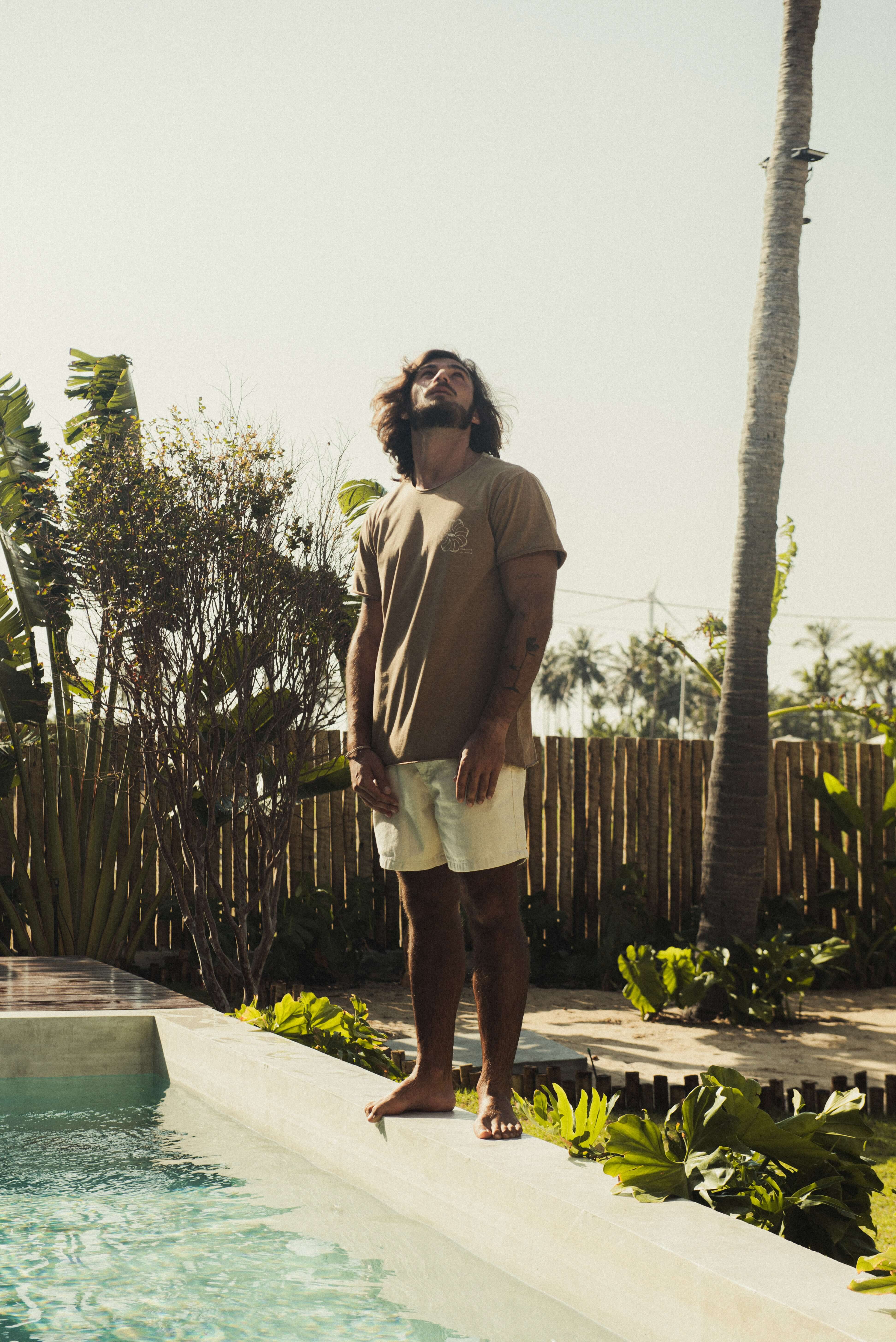 Homem ao ar livre vestindo Camiseta Stone Feel The Winds - Marrom da Greenish, com toque macio e visual rústico em um ambiente tropical.