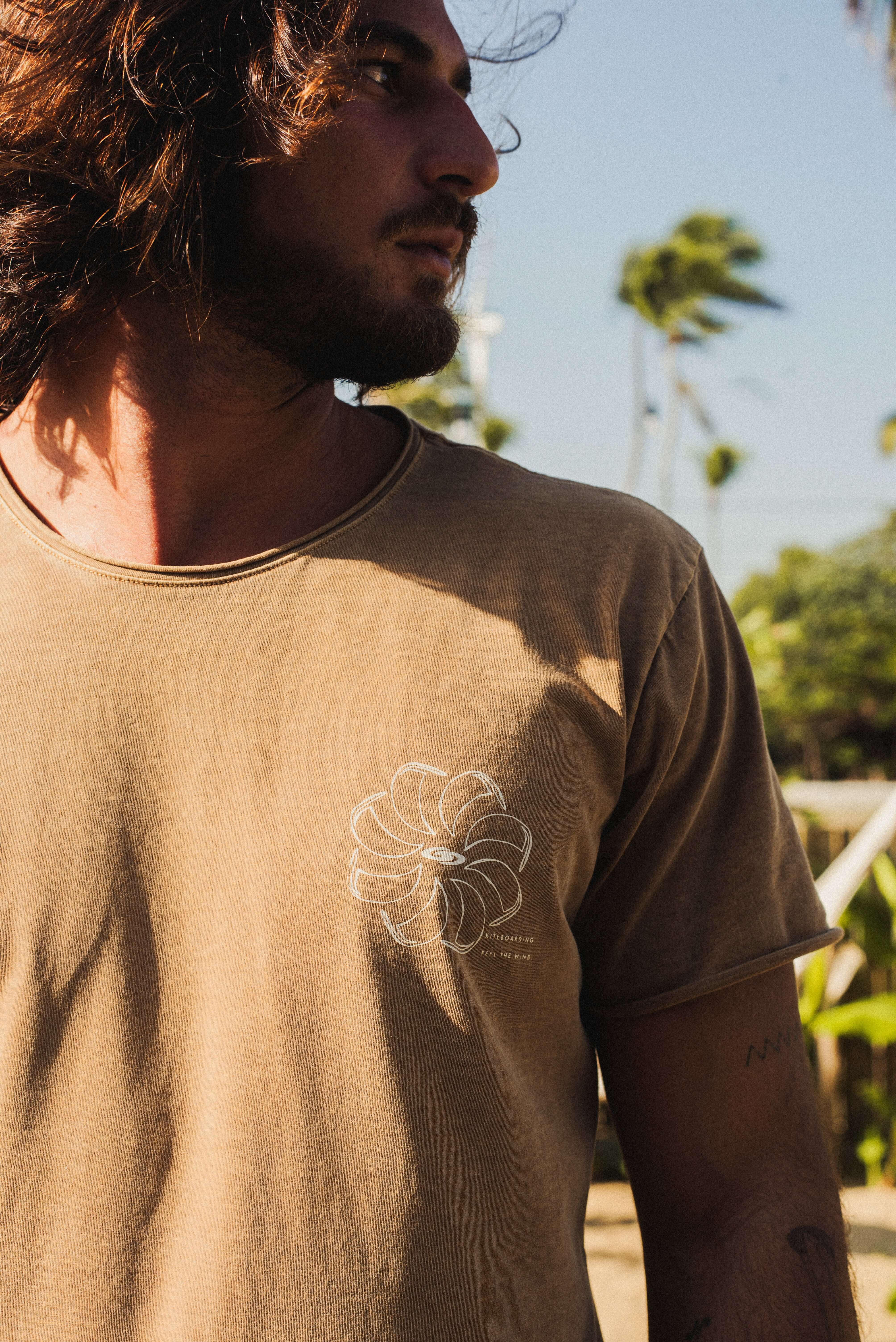 Camiseta Stone Feel The Winds - Marrom, Greenish, em algodão com visual rústico e estampada, usada por homem ao ar livre com vento.