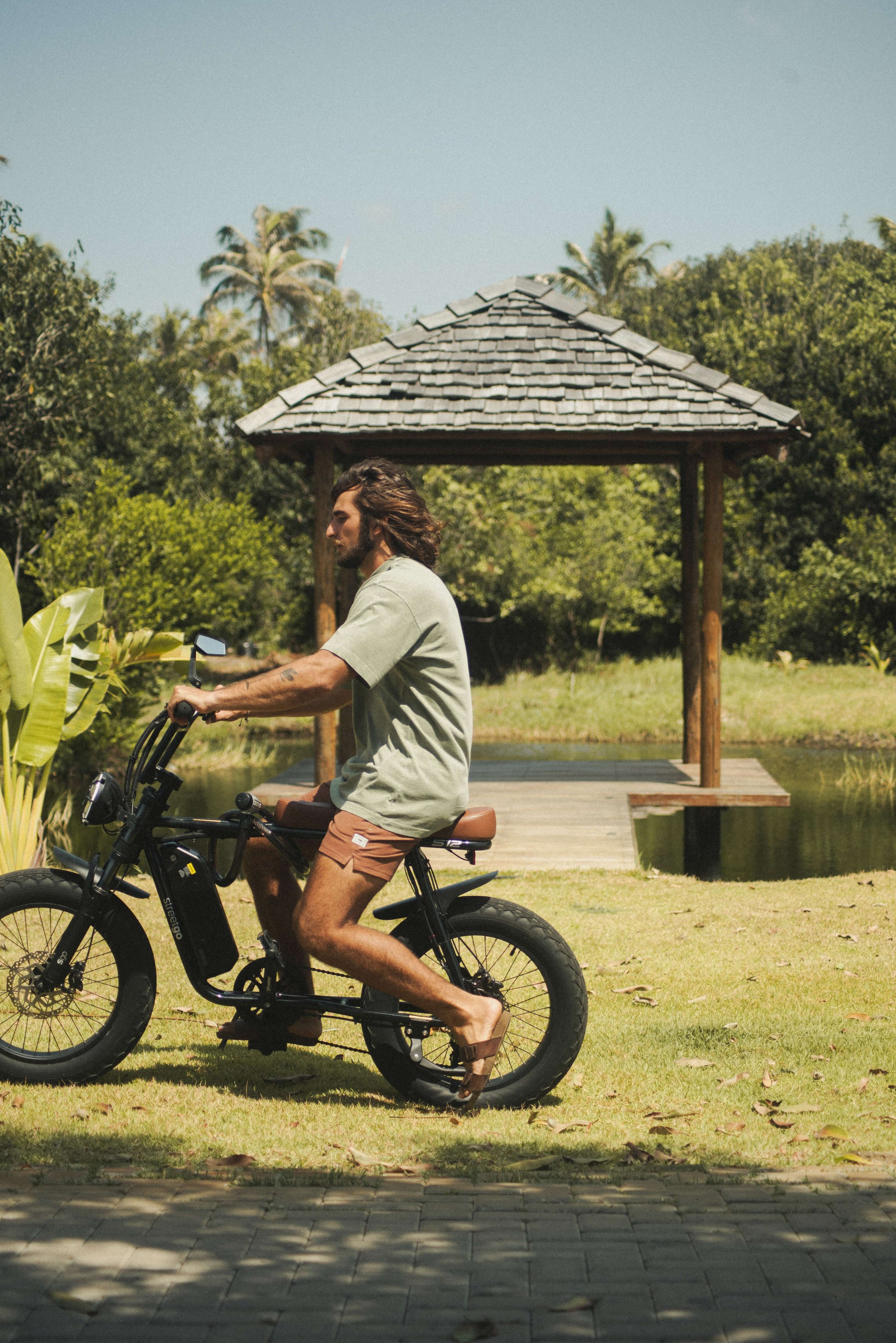Homem usando Camiseta Stone Oversized Greenish - Verde da marca Greenish pedalando tranquilamente ao ar livre.