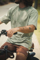 Jovem em bicicleta vestindo Camiseta Stone Oversized Greenish - Verde da Greenish, estilo vintage com caimento solto e toque aveludado.