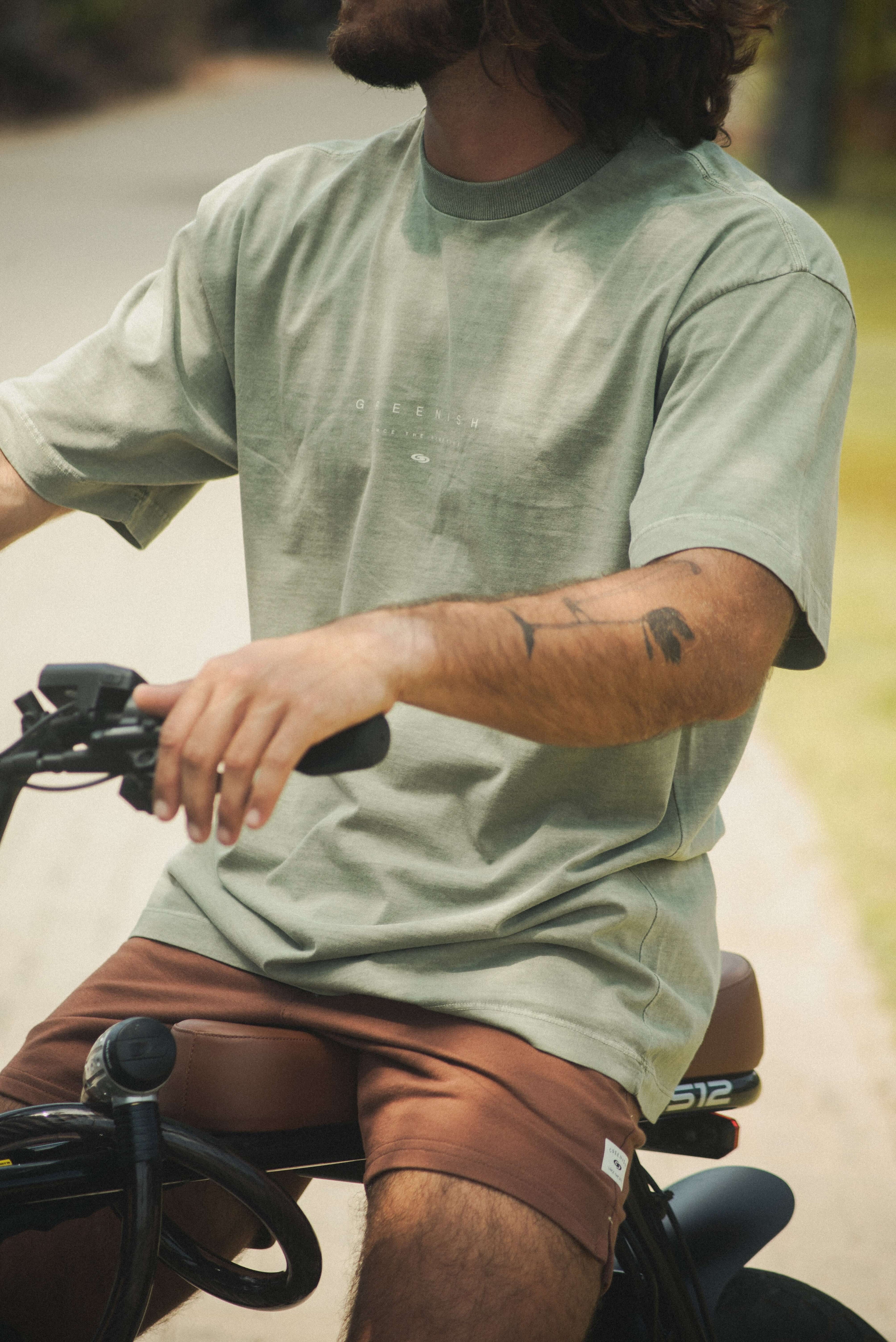 Jovem em bicicleta vestindo Camiseta Stone Oversized Greenish - Verde da Greenish, estilo vintage com caimento solto e toque aveludado.