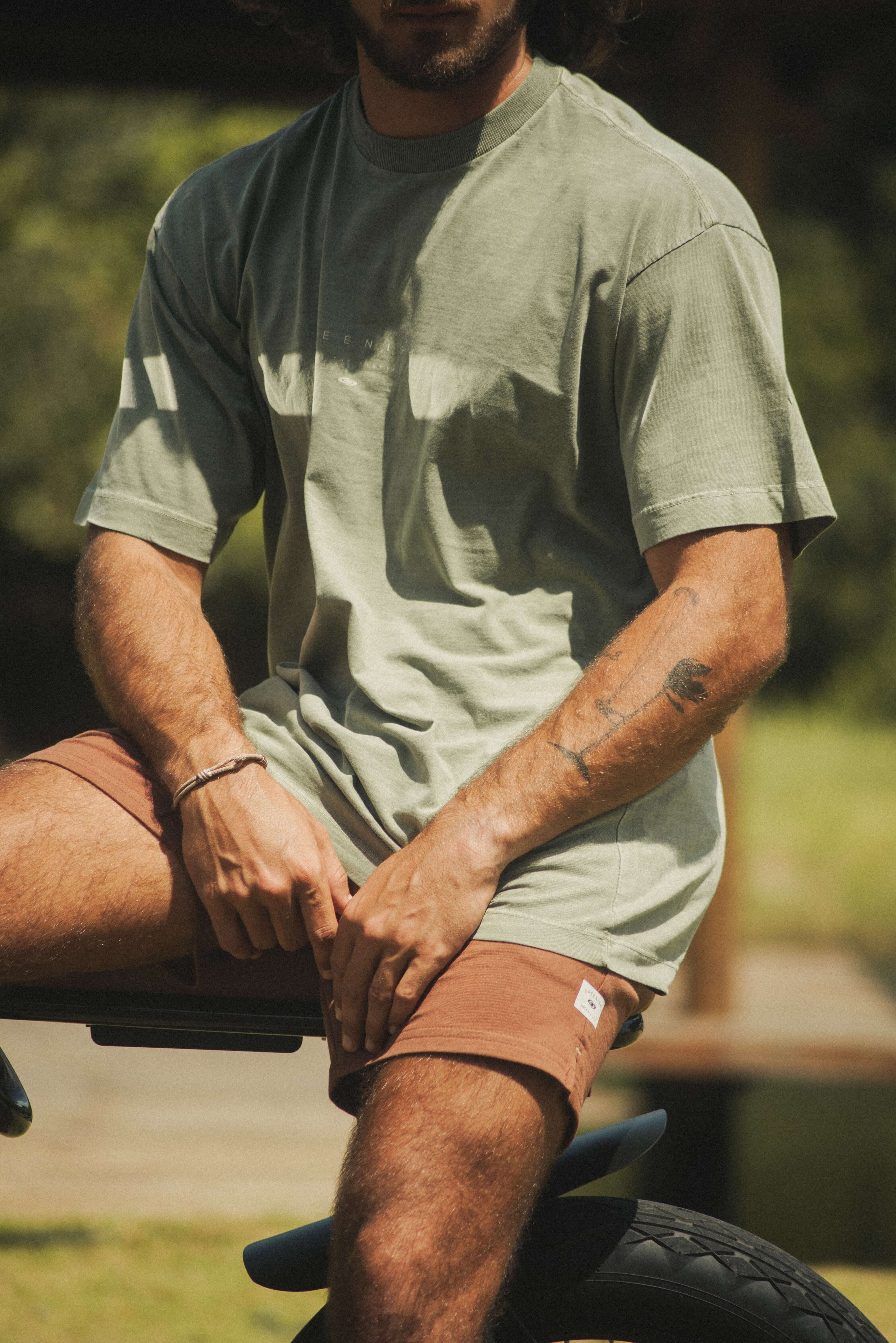 Homem vestindo Camiseta Stone Oversized Greenish - Verde da marca Greenish, em ambiente ao ar livre, com design moderno e estilo vintage.