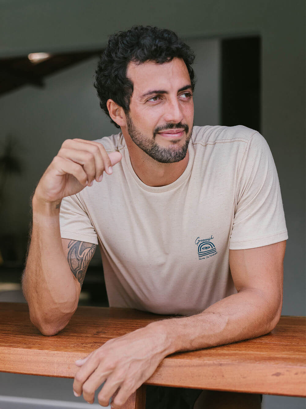 Homem vestindo camiseta Sunset bege da marca Greenish, posando em ambiente natural.