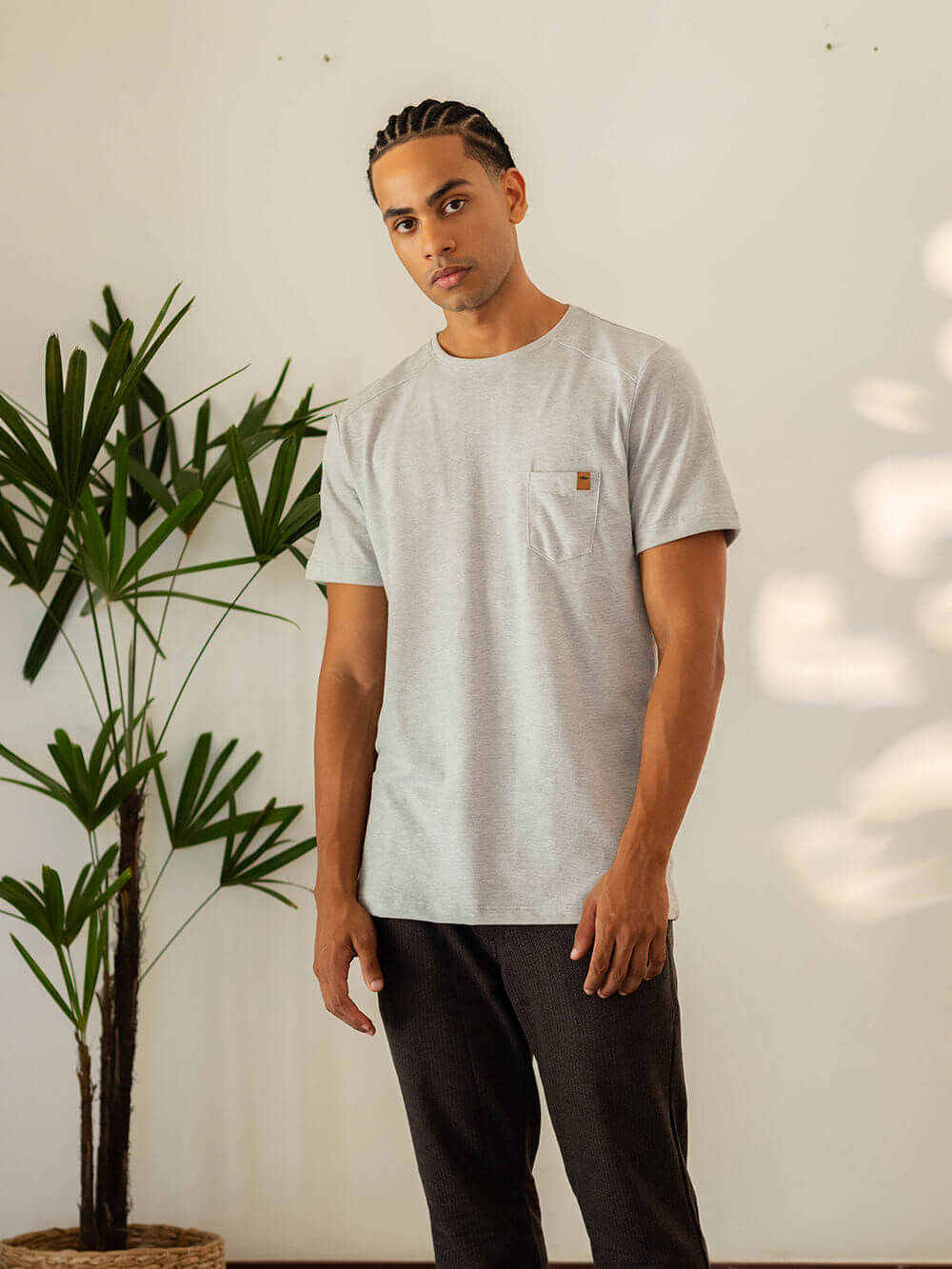 Camiseta TURN cinza da Greenish, modelo masculino posando em ambiente com plantas.
