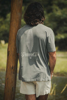 Homem vestindo a Camiseta Oversized Stong Leaf Plank - Chumbo da Greenish, com estampa de folha e logo, em um ambiente natural.