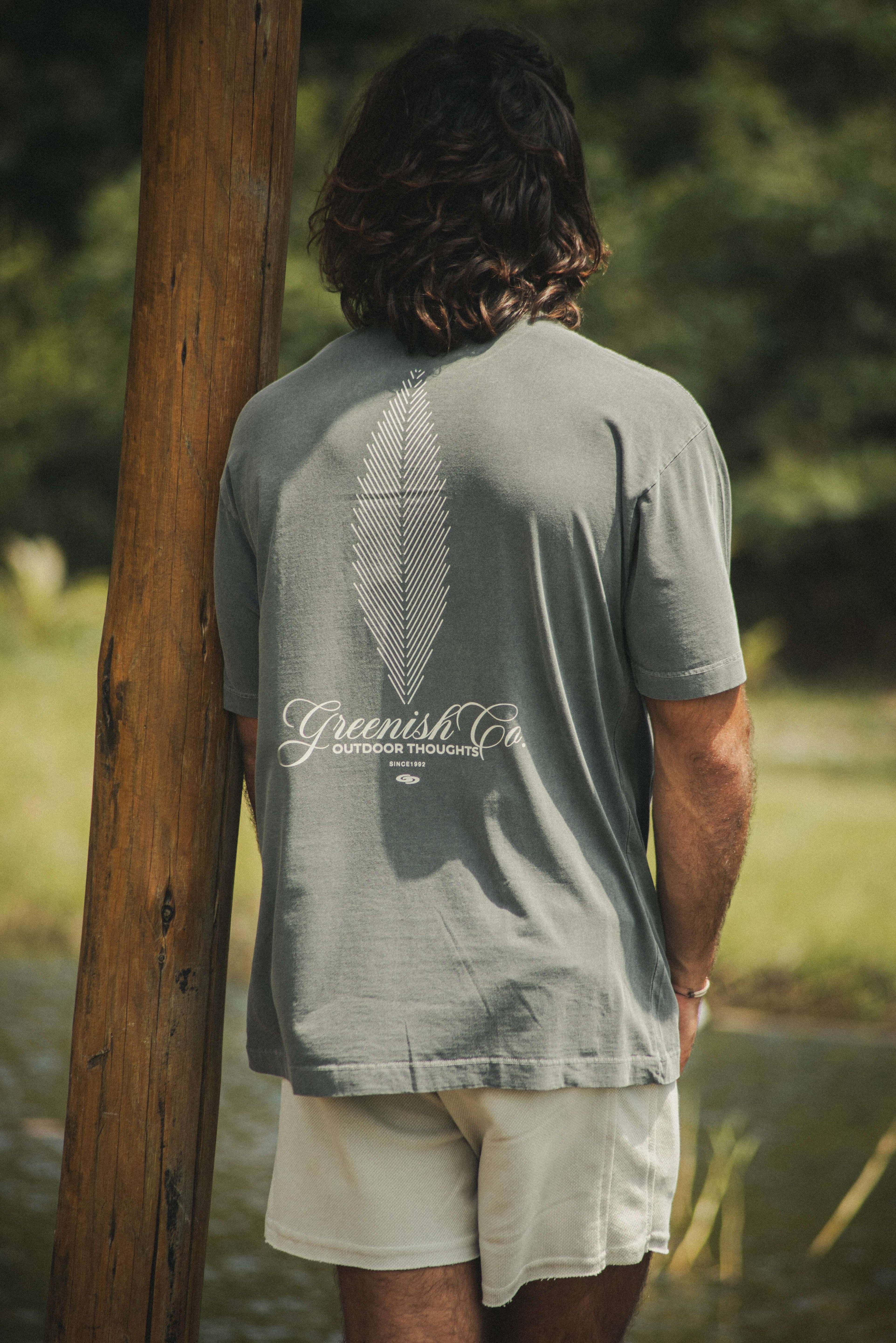 Homem vestindo a Camiseta Oversized Stong Leaf Plank - Chumbo da Greenish, com estampa de folha e logo, em um ambiente natural.