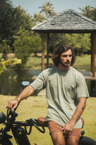 Homem vestindo Camiseta Stone Oversized Greenish - Verde, da marca Greenish, sentado em uma bicicleta ao ar livre.