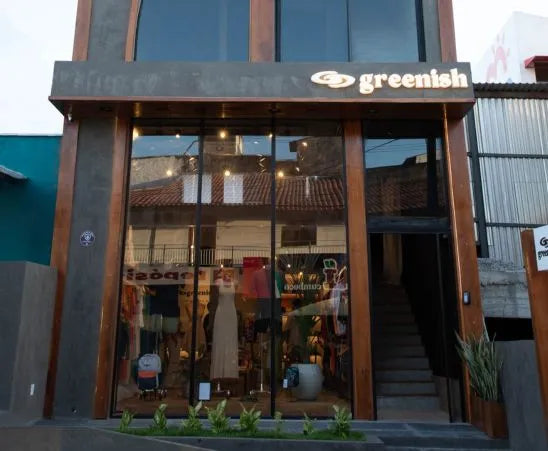 Fachada da loja Greenish, com grandes janelas exibindo roupas e decoração interna moderna.