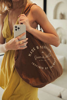 Jovem com Ecobag Greenish - Marron de algodão, alças duráveis e estampa "Made by Surfers", refletindo autenticidade. Marca: Greenish.