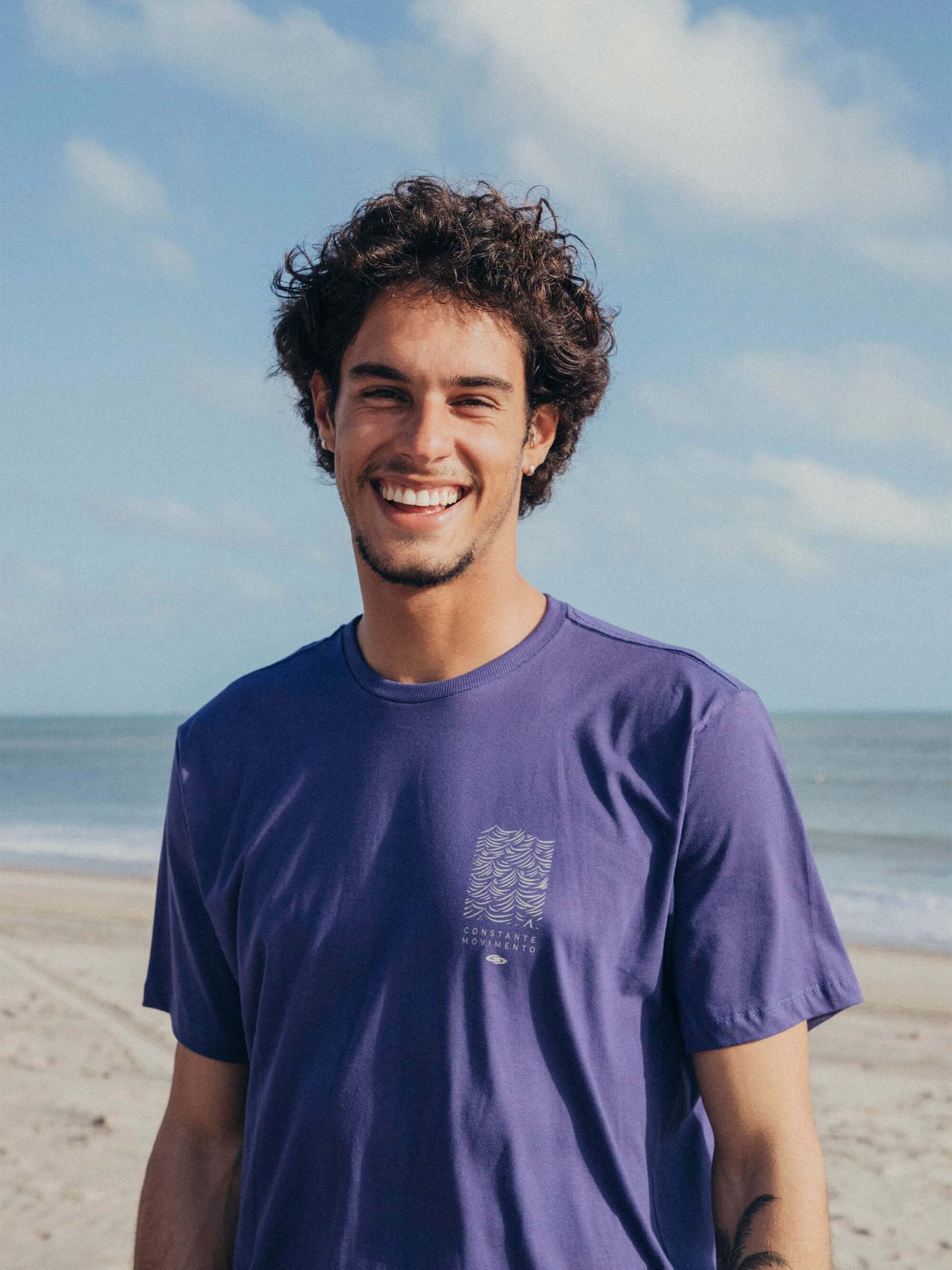 Camiseta Constantemente Movimento azul royal da marca Greenish, modelo em foto, à beira da praia.