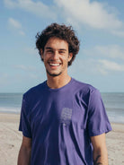 Camiseta Constantemente Movimento azul royal da marca Greenish, modelo em foto, à beira da praia.
