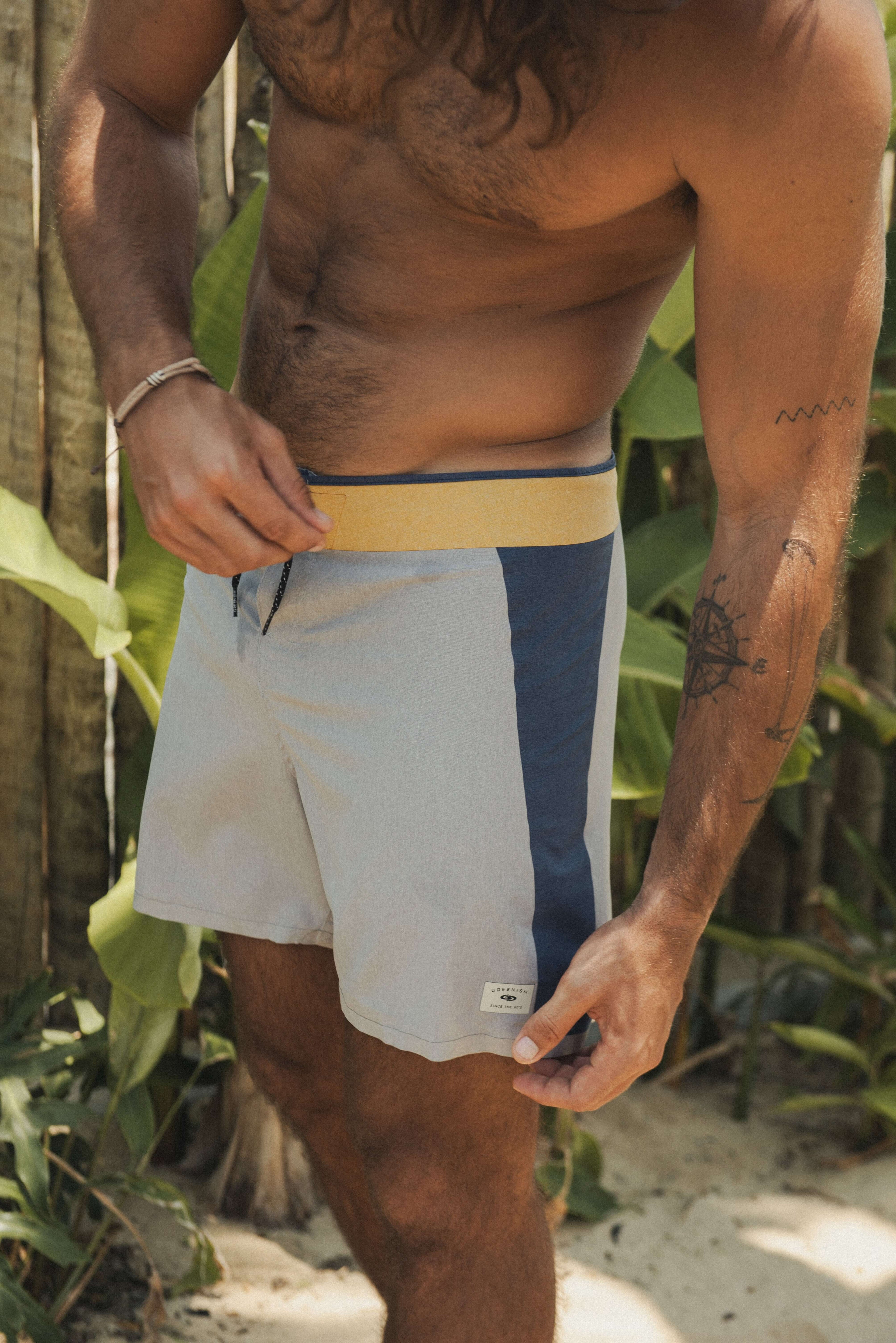 Homem usando BOARDSHORTS ULTRALIGHT II SUNSET - CINZA Greenish em um ambiente tropical, destacando o design leve e multicolorido.