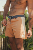 Homem vestindo BOARDSHORTS ULTRALIGHT II SUNSET - CAQUI, frente a folhagem verde. Estilo e resistência por Greenish.