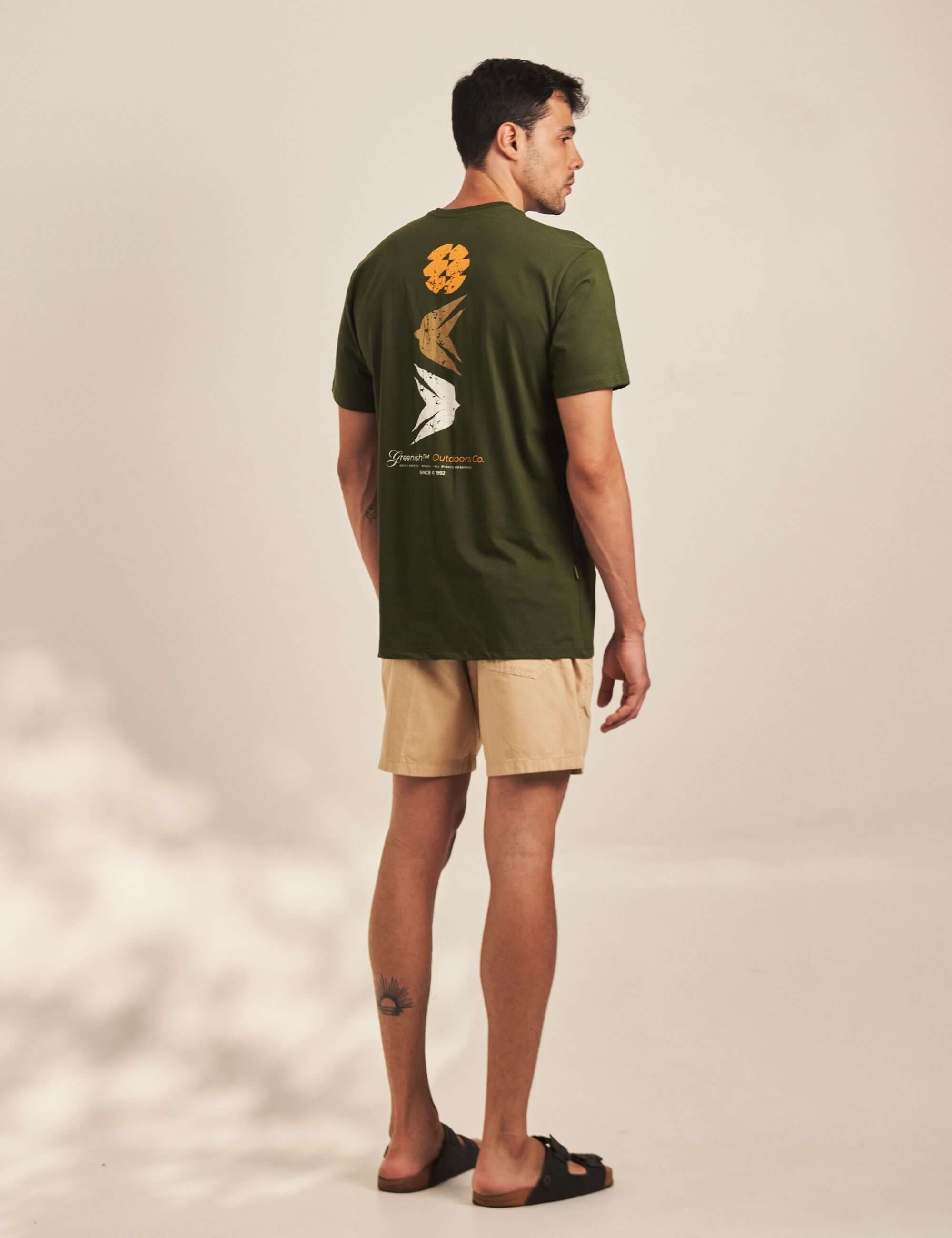 Alt Tag: Camiseta To Somewhere - Verde Escuro da Greenish vista por trás com silk costado, modelo masculino em ambiente outdoor casual
