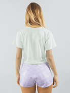 Camiseta cropped verde clara da marca Greenish, vista de trás, combinando com shorts lilás estilo tie-dye.