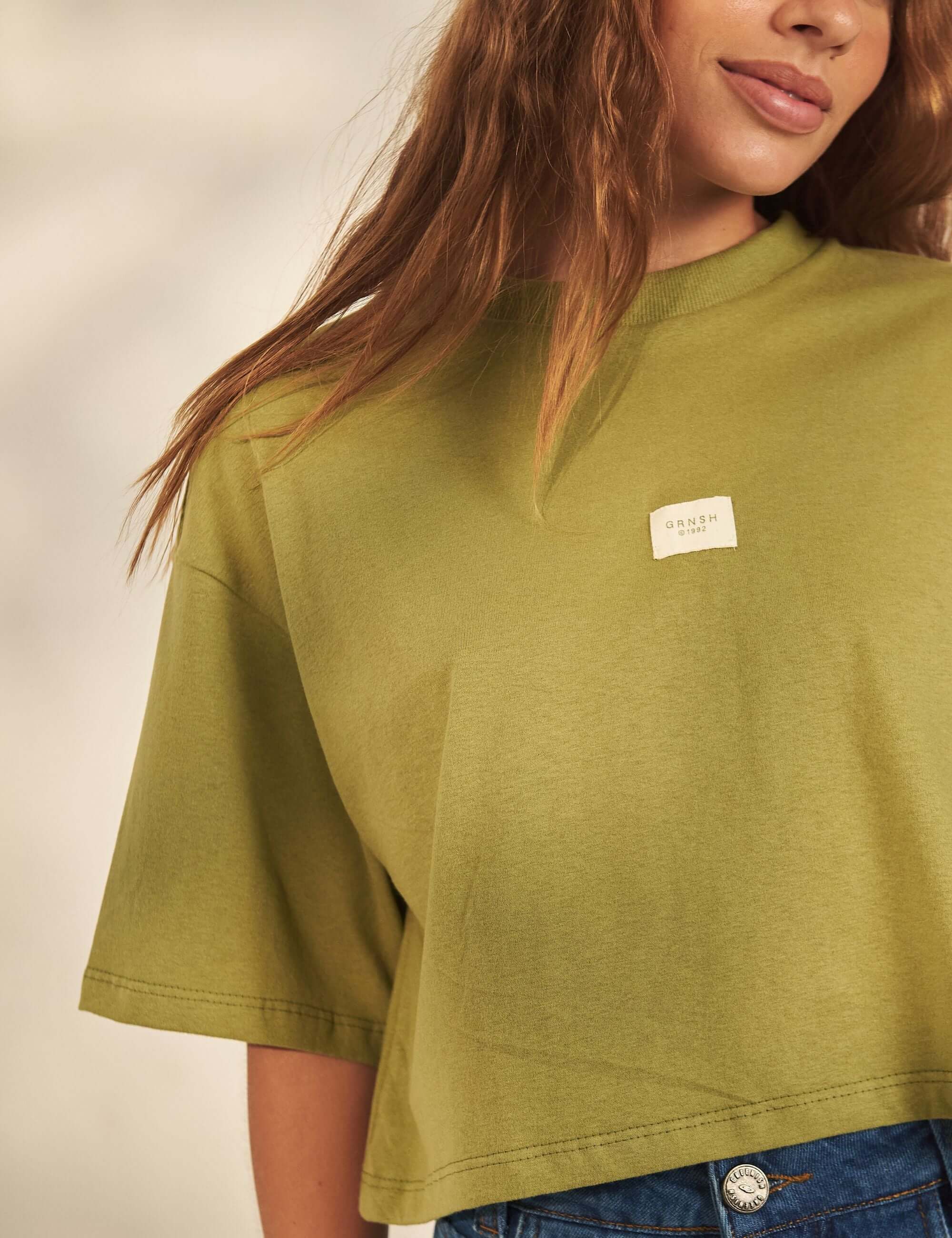 Alt Tag: Cropped Oversized Grnsh - Verde da Greenish em malha algodão, modelagem ampla cropped com etiqueta frontal e gola em ribana