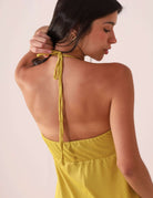 Mulher usando Macaquinho Curto Flora - Amarelo mostrando detalhe das costas com amarração, ideal para dias ensolarados.