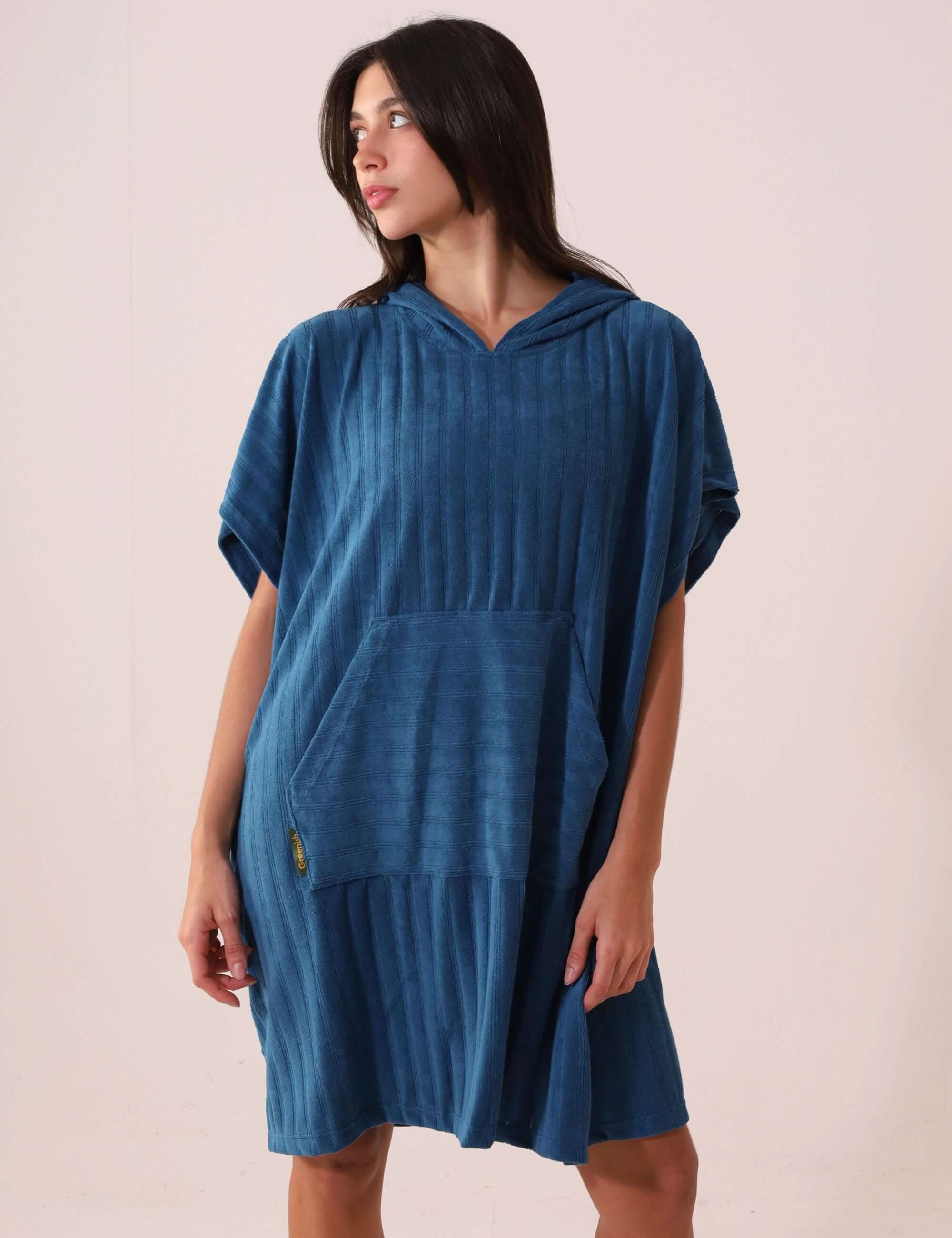 Mulher usando PONCHO CURTO CANELADO - AZUL da Greenish, com bolso estilo canguru, ideal para praia e esportes aquáticos.