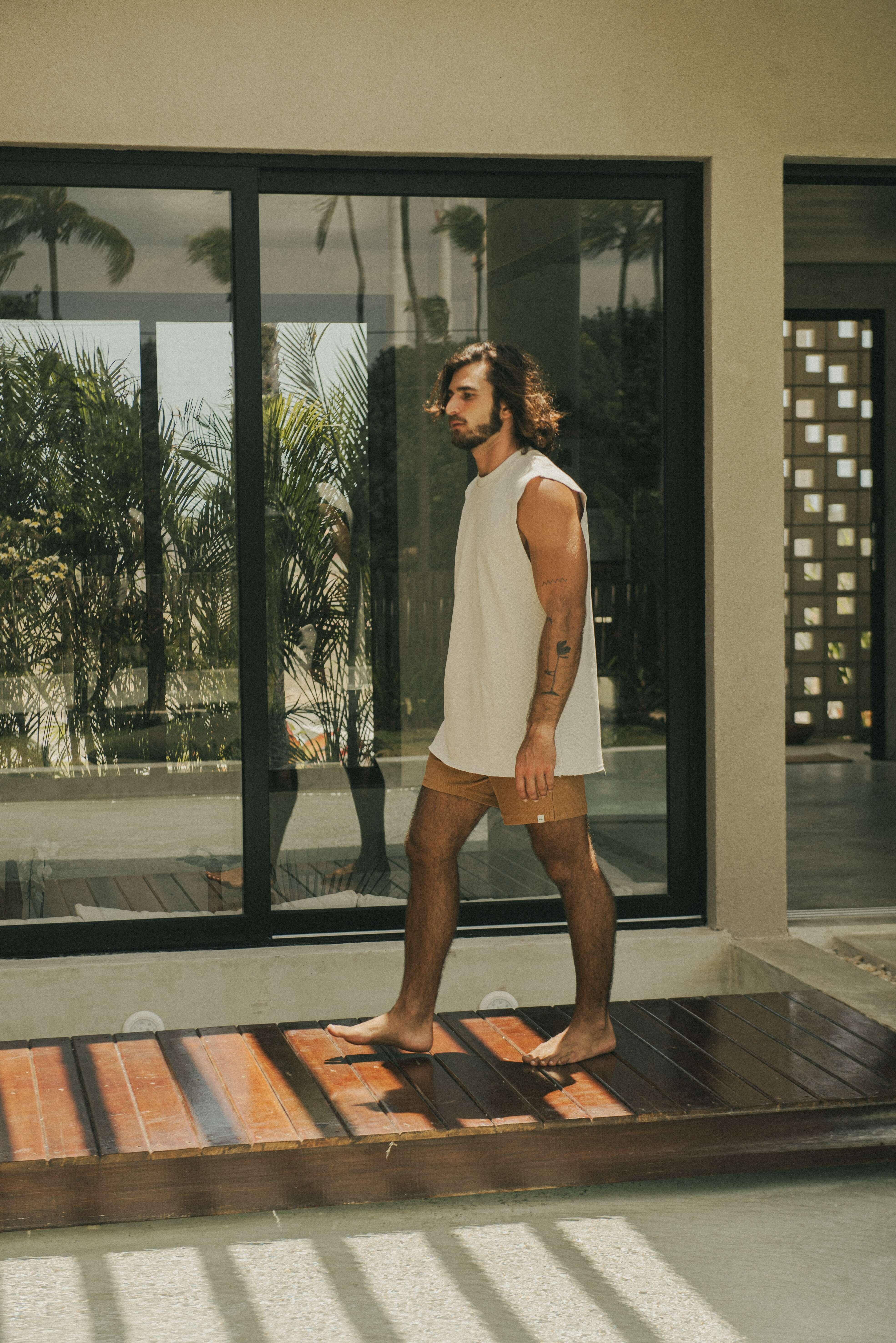 Homem usando Regata Larga Waves - Bege da marca Greenish em uma varanda ensolarada.