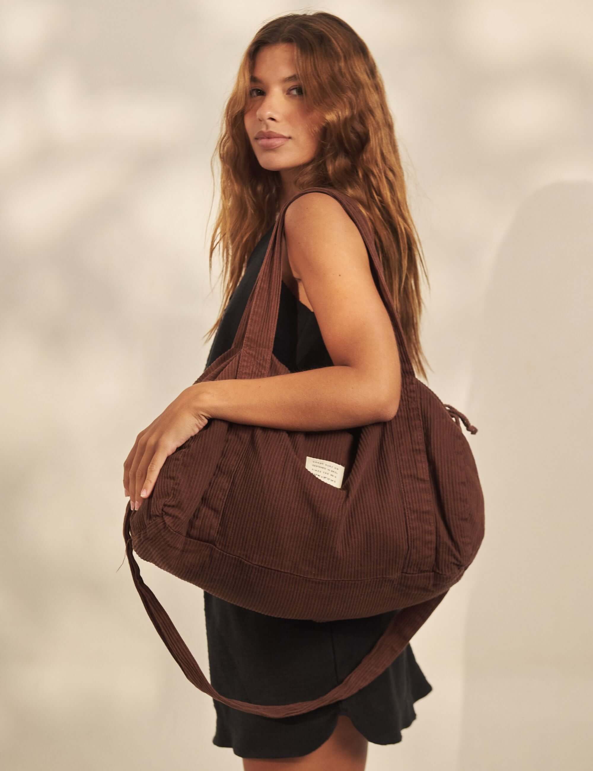 Saia Curta Sunset - Preto da Greenish em cenário praia casual, modelo com bolsa marrom e look preto, saia curta versátil e cintura alta