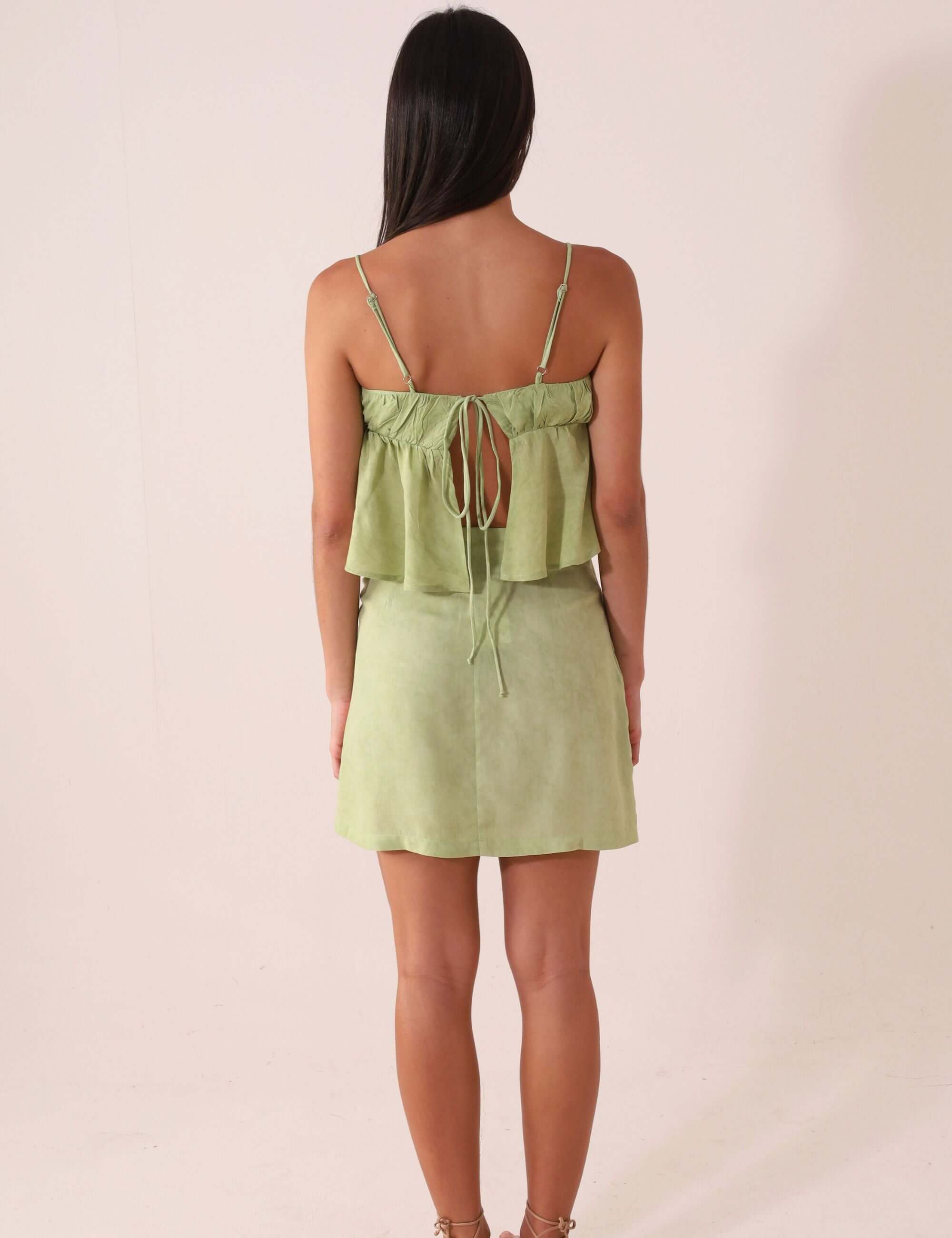 Modelo de costas vestindo SAIA CURTA THÁ - VERDE da Greenish com amarração lateral e toque macio em viscose.