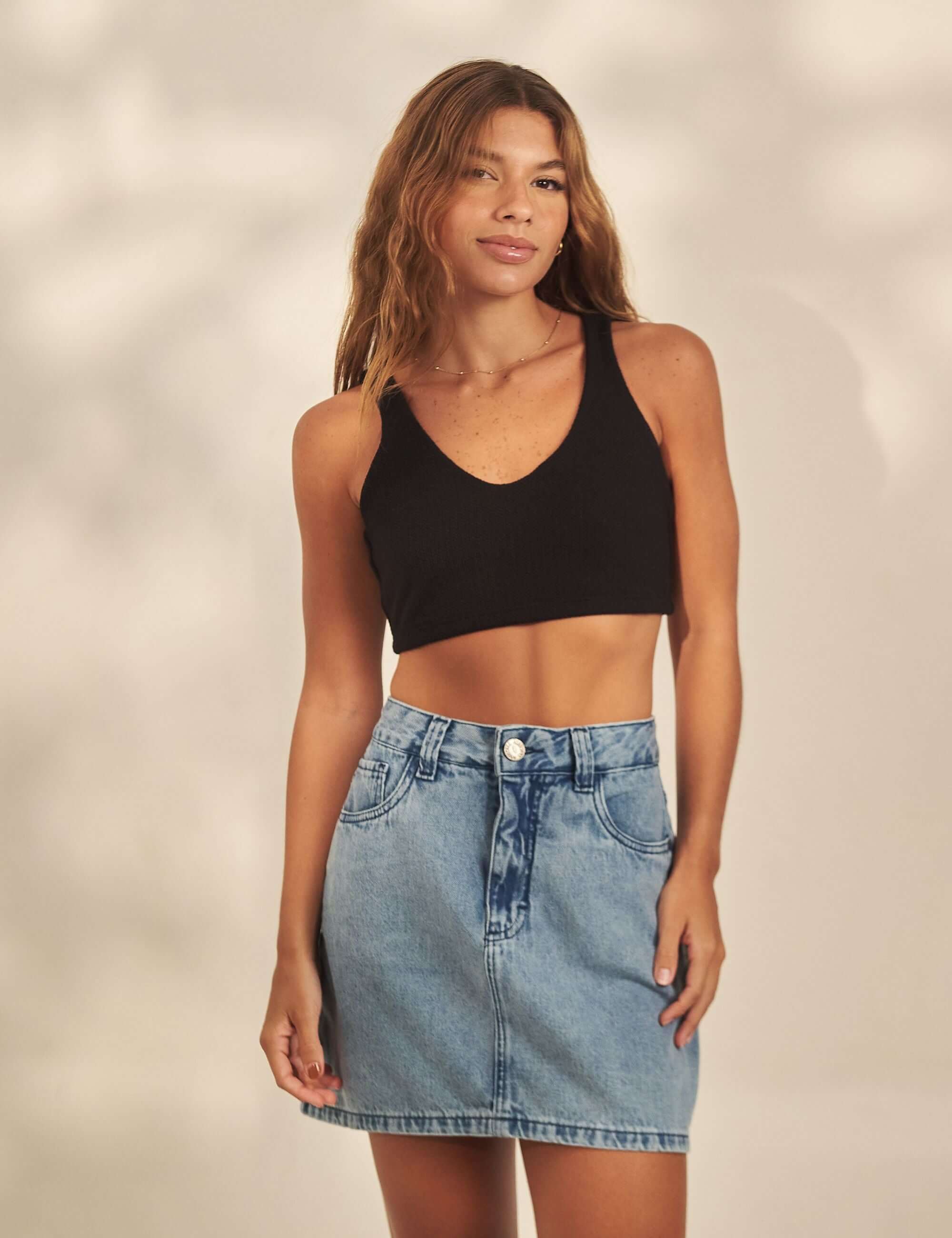 Model wearing Greenish Saia Curta Jeans Classic, featuring a low waist, indigo wash, double waistband, and applied pockets.