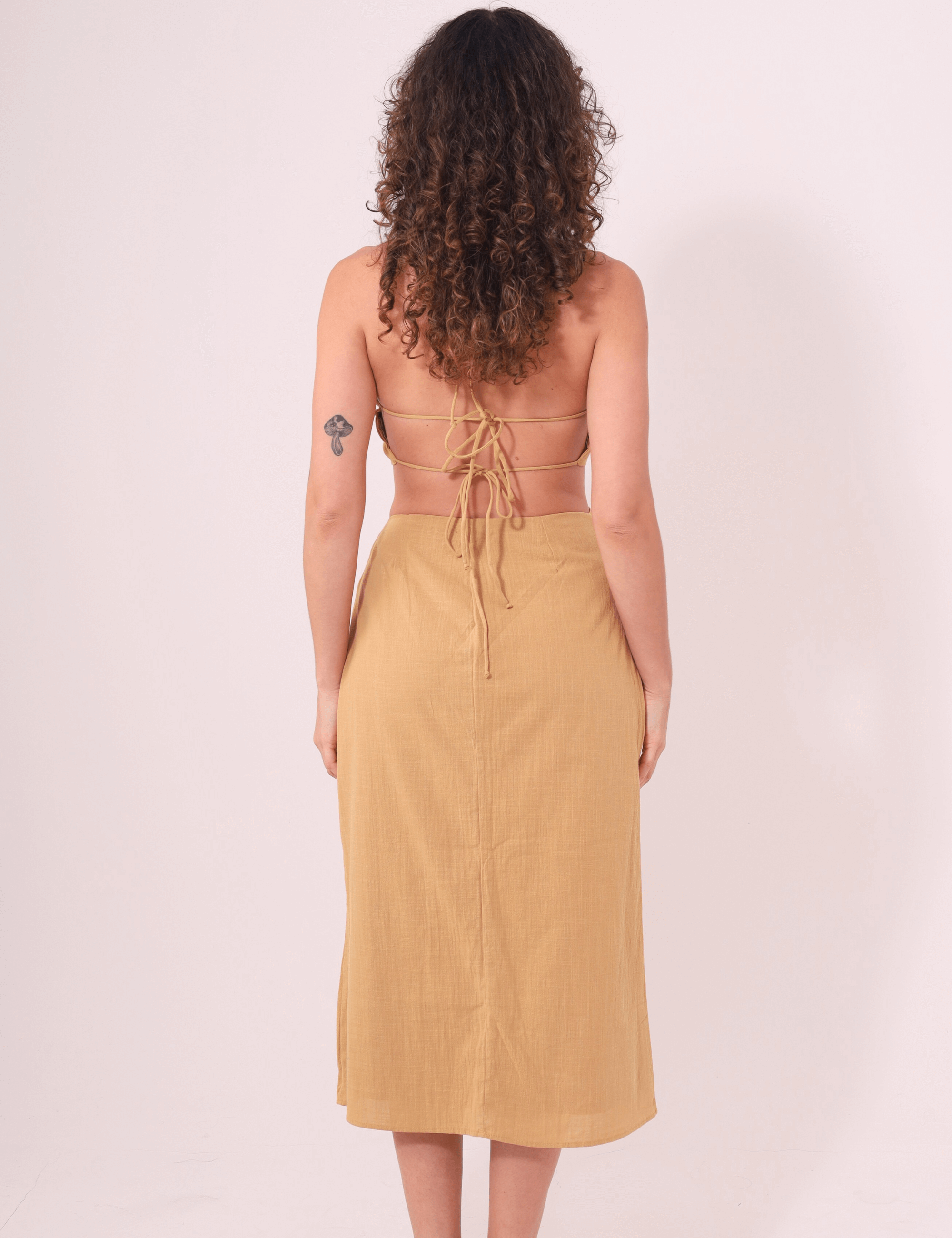 Mulher vestindo Saia Midi Sunny Caqui da Greenish, de costas, destacando o ajuste na cintura e tecido leve para dias de sol.